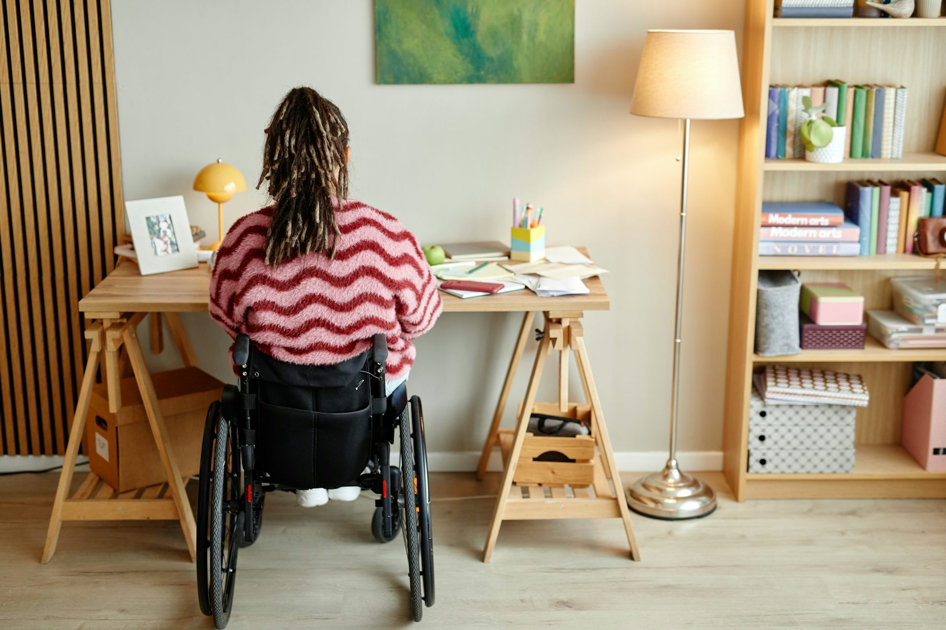 Une femme en fauteuil, vue de dos, travaille à son bureau.