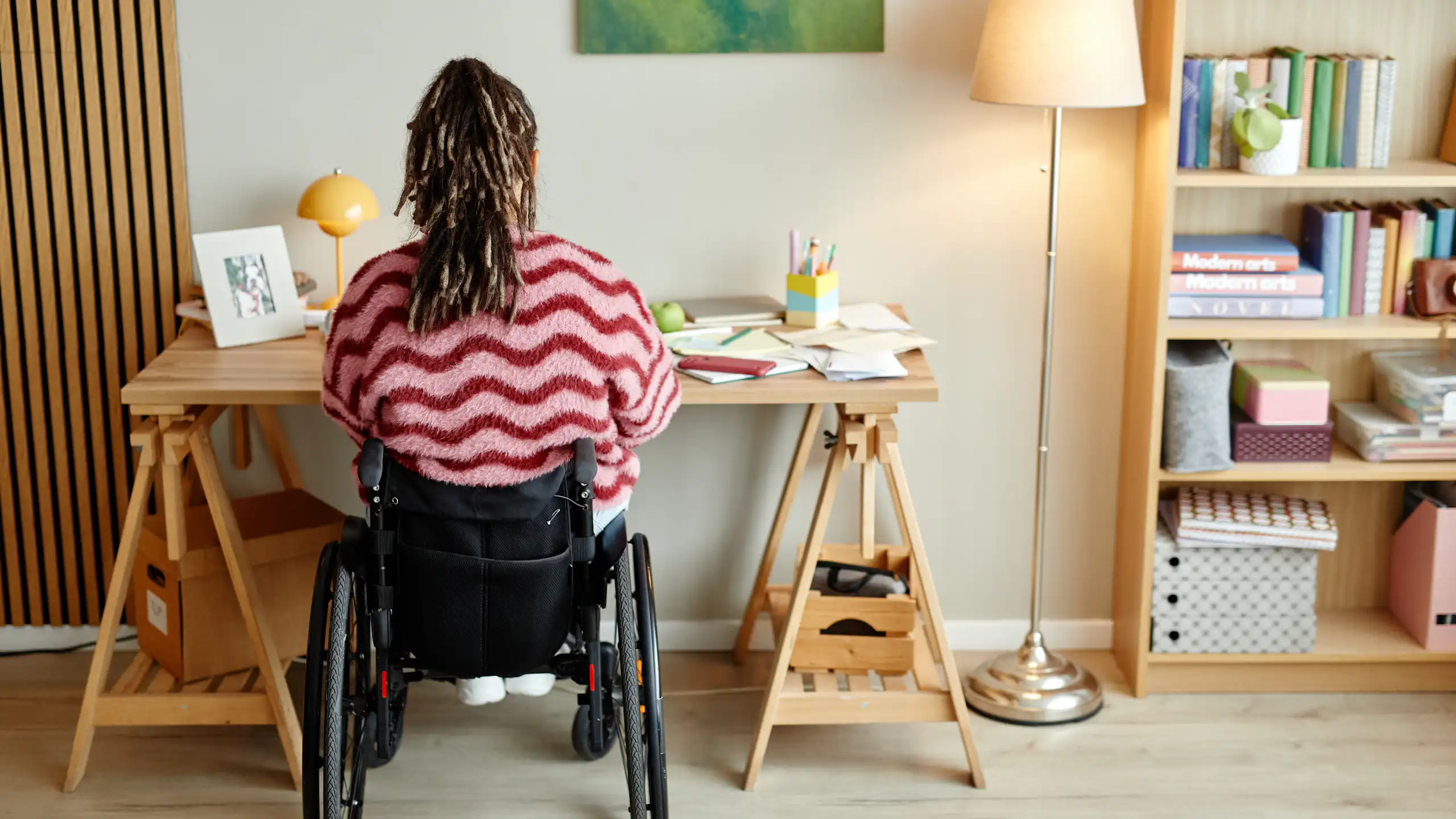 Une femme en fauteuil, vue de dos, travaille à son bureau.