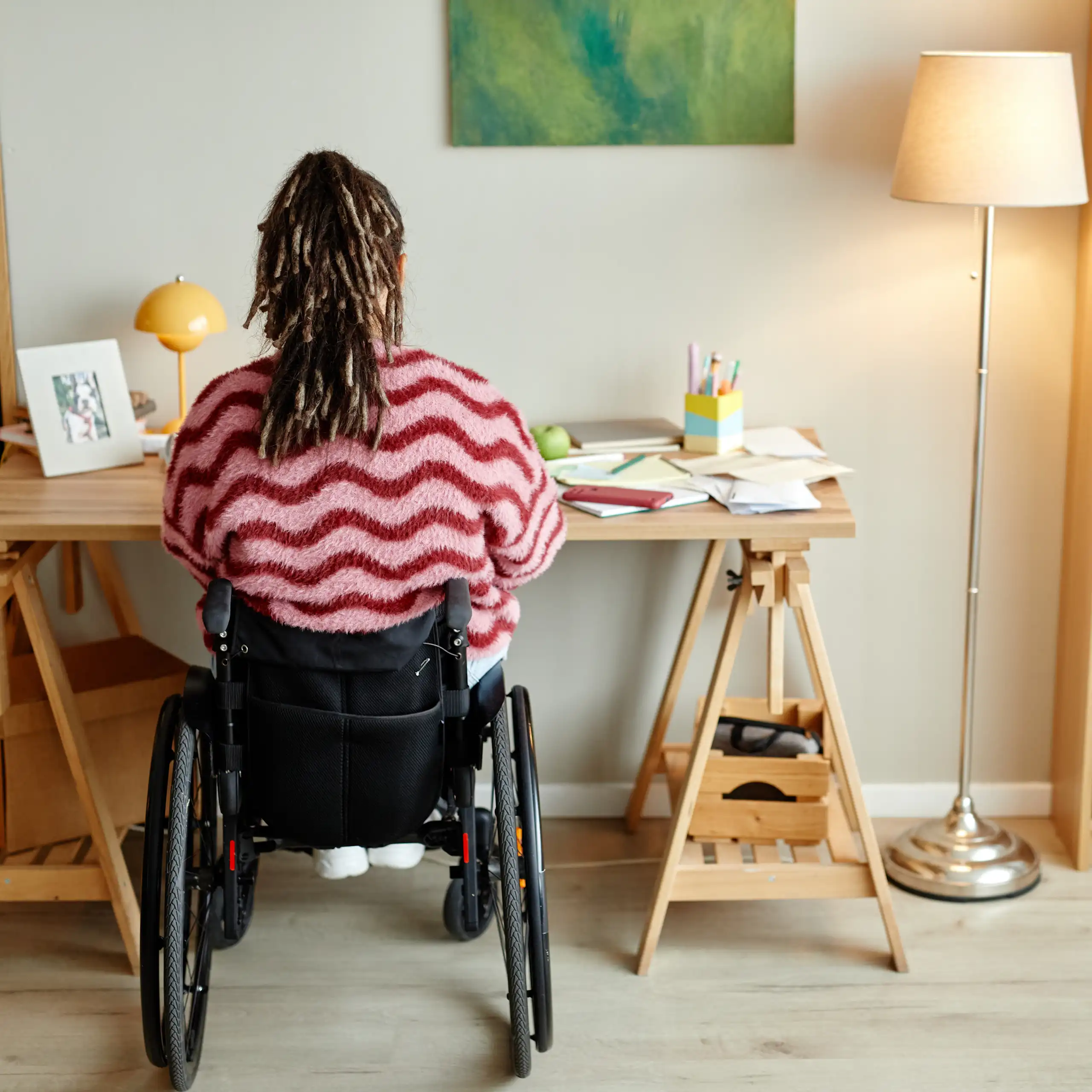 Une femme en fauteuil, vue de dos, travaille à son bureau.