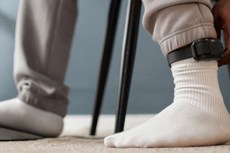 Ankle monitor on the ankle of a person wearing grey sweatpants and socks