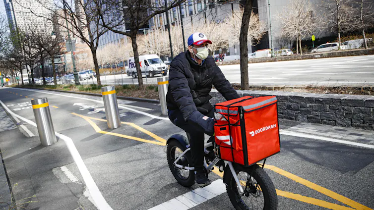 A Doordash worker with a face mask rides his bicycle along a path on the West Side Highway in New York City during the COVID pandemic.