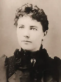 Black and white portait of a woman with her hair in a bun wearing a 19th century-style dress with a high ruffled neck.