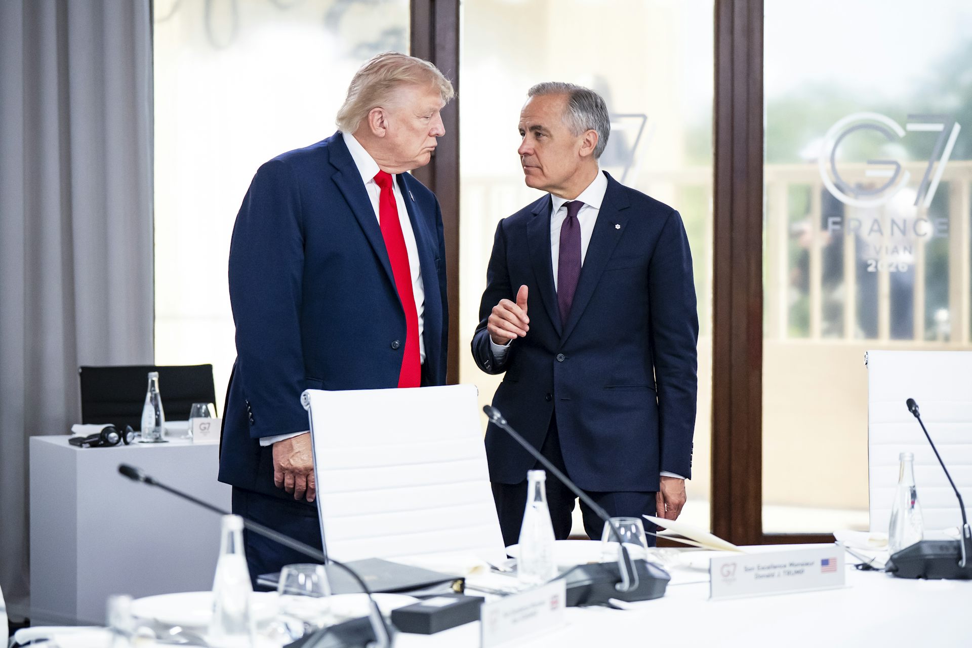 Donald Trump et Mark Carney discutent ensemble, debout devant une table.