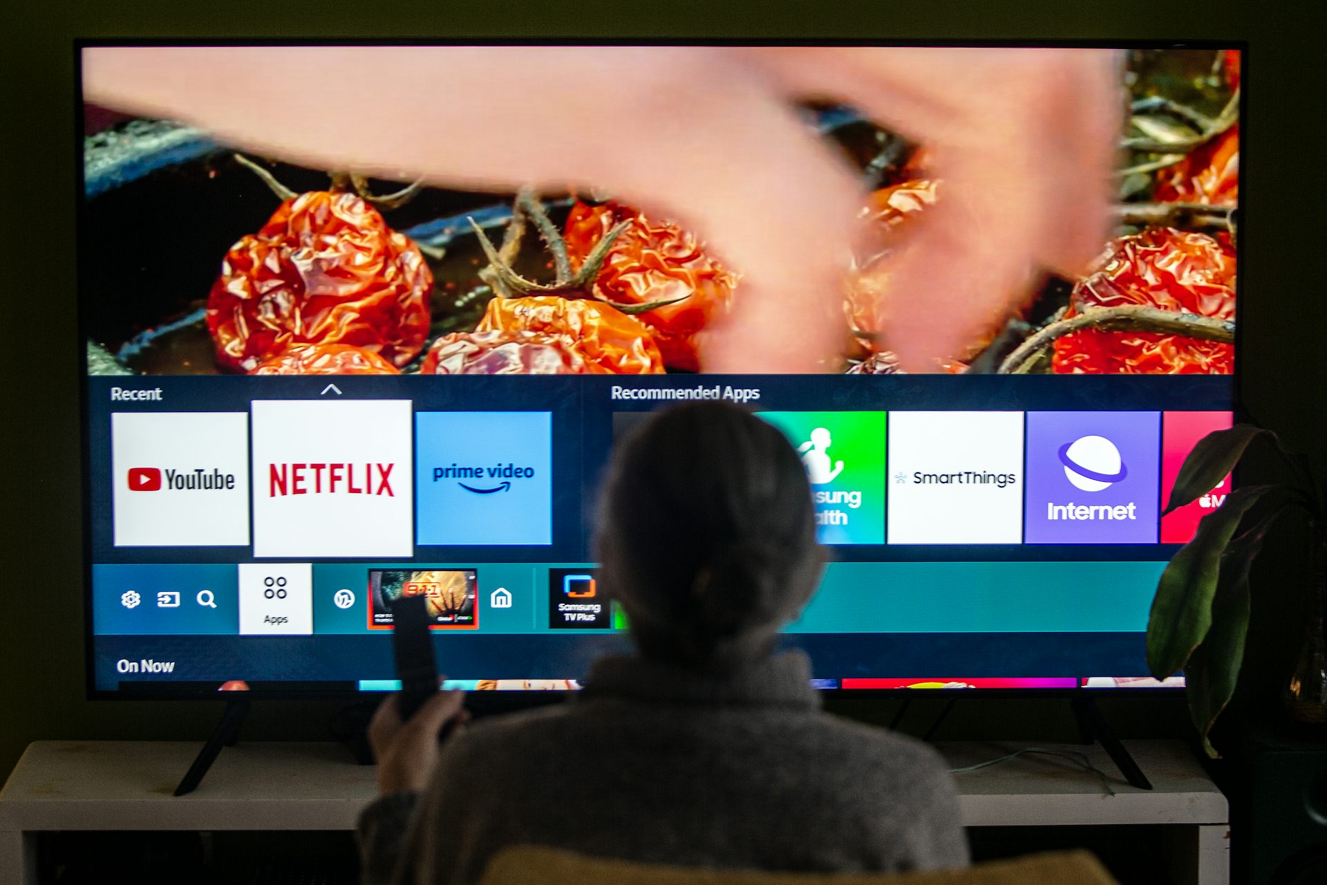 Someone holds a remote control in front of a television screen displaying icons for accessing various platforms, including Netflix, Amazon Prime, and YouTube
