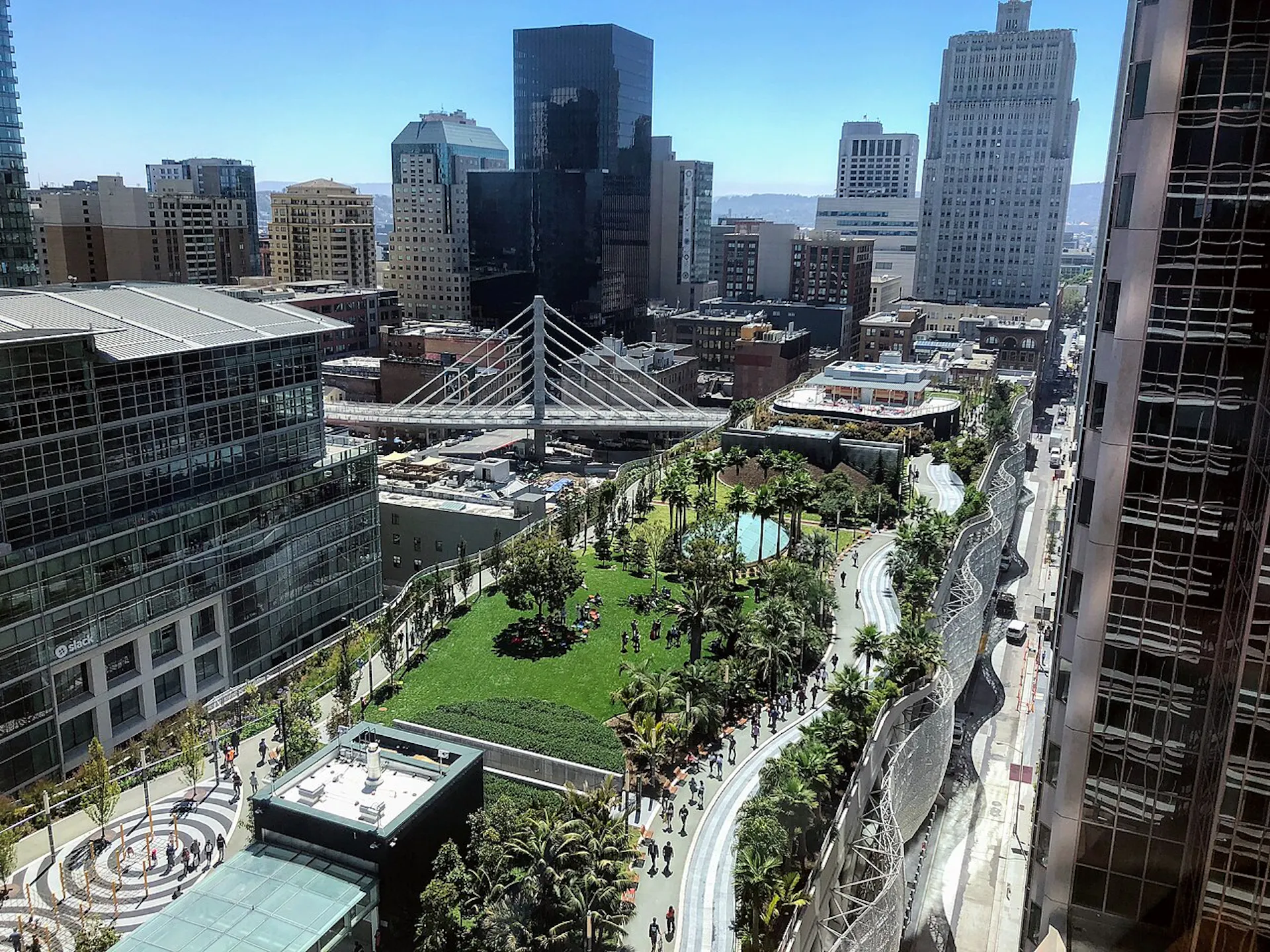 A blocks-long park several stories up, with people sitting on a green and walking on paths.