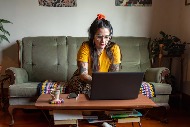 Tattooed woman on velvet couch looks at laptop.