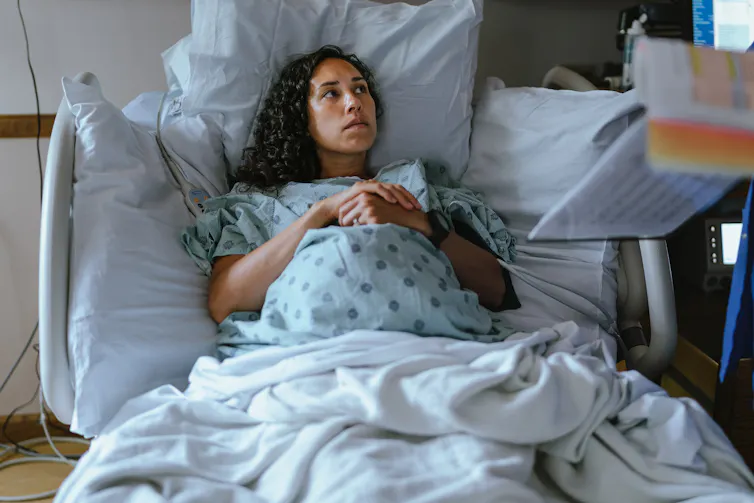 A pregnant woman lays in a hospital bed, deep in tought