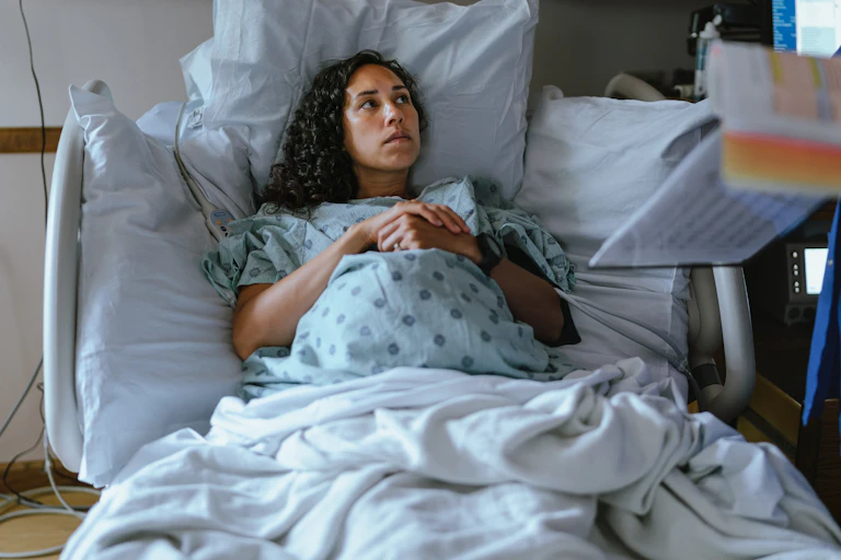A pregnant woman lays in a hospital bed, deep in tought