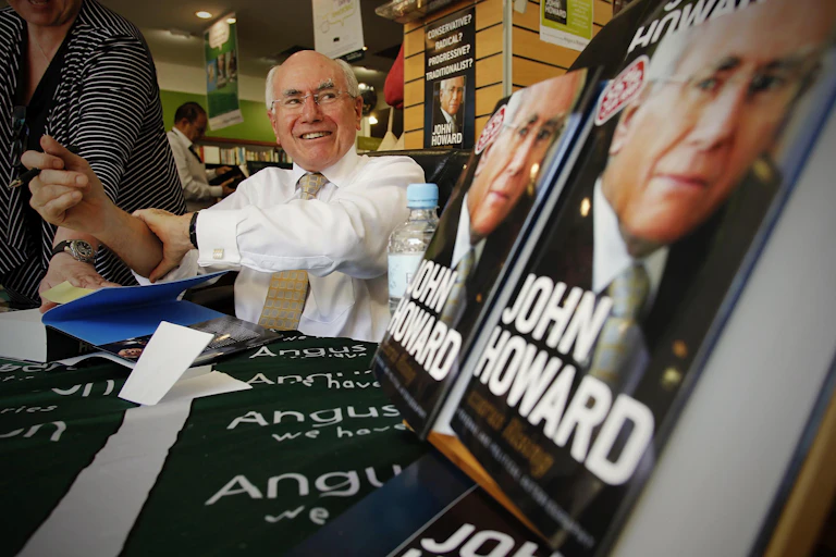 John Howard grinning with copies of his book