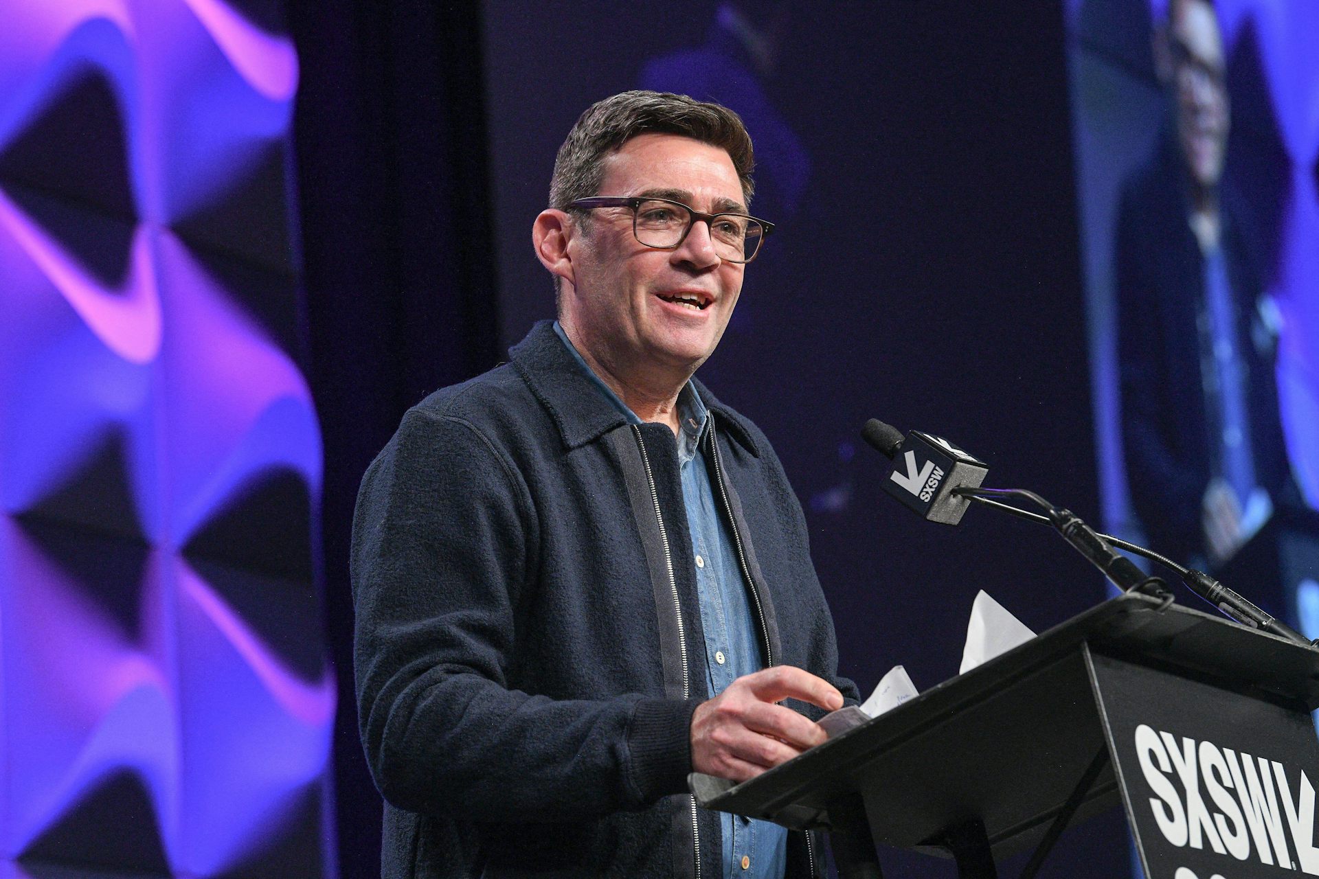 A man smiling as he stands at a podium at a conference.