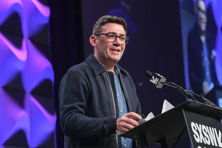 A man smiling as he stands at a podium at a conference.