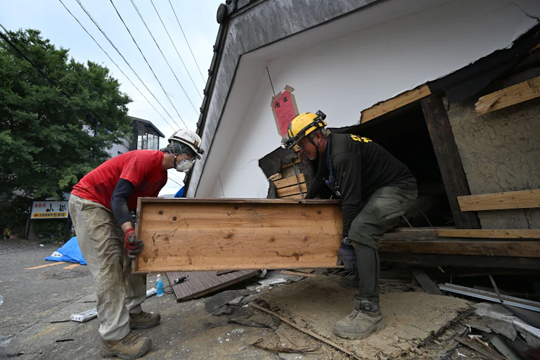 Two people try to carry a large chest out of a collapsed building in Japan, after an earthquake.