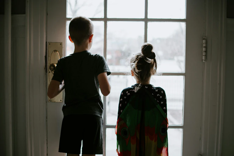 Two children seen from behind looking out a glass-paned door