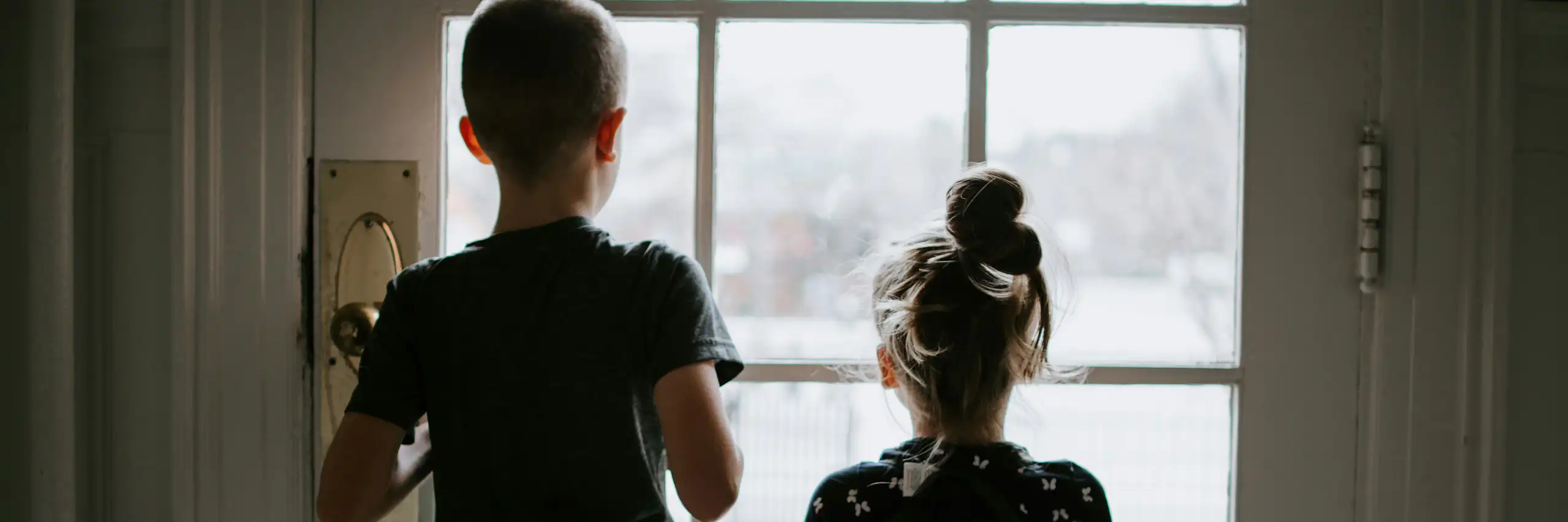 Two children seen from behind looking out a glass-paned door