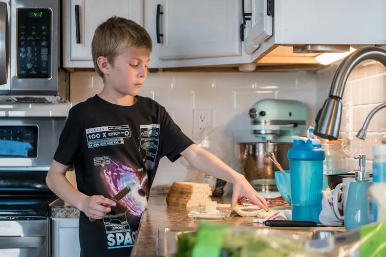 A boy in a t-shirt buttering bread at a kitchen counter