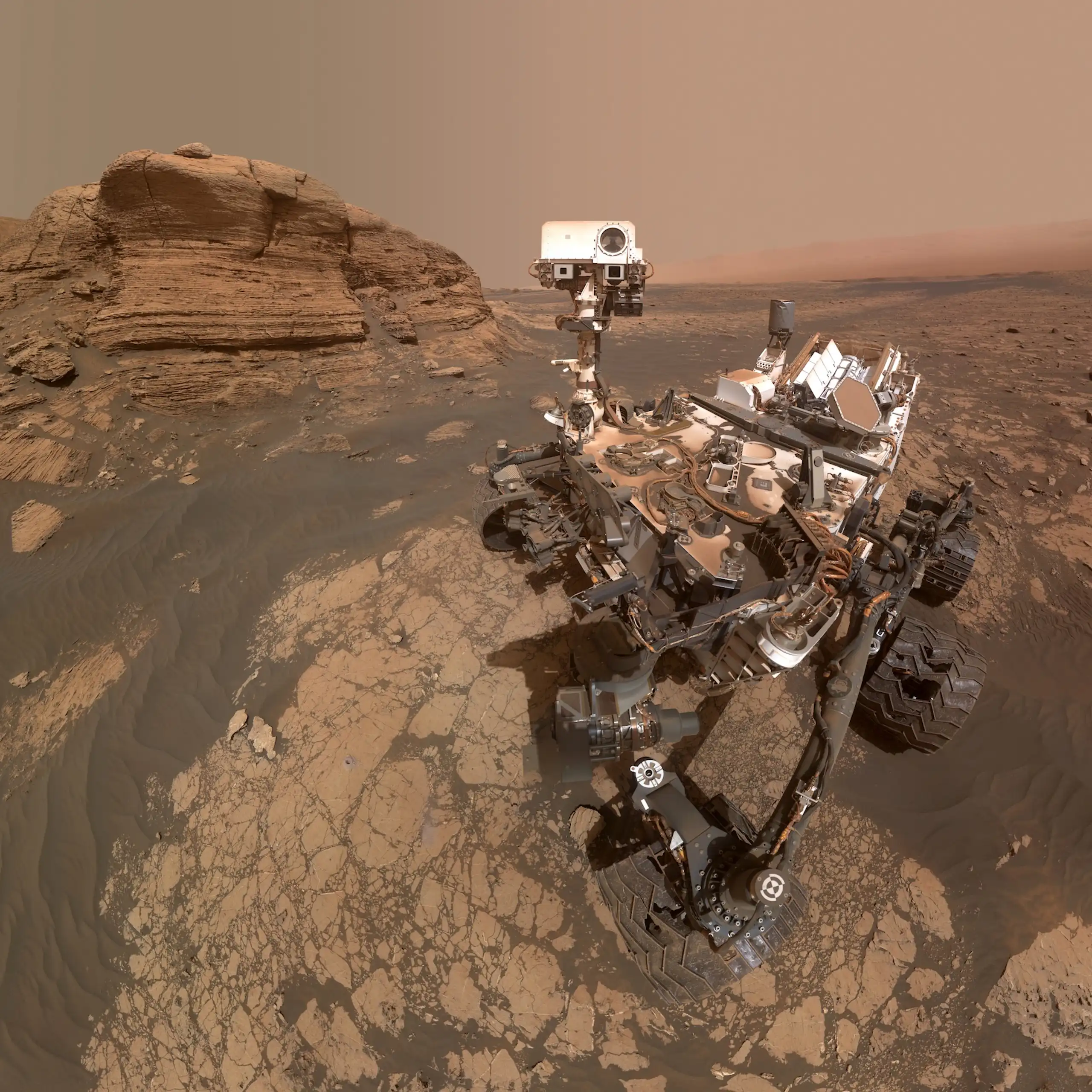 The Curiosity rover is parked in front of rock outcrops on Mars.