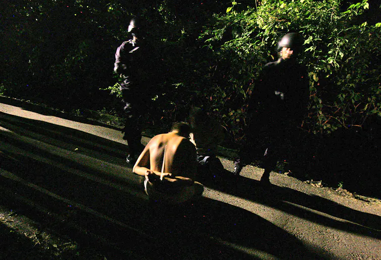 Two men in uniform stand guard over a man in handcuffs.