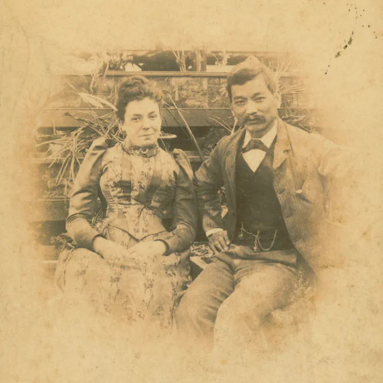 Sepia coloured photograph of a couple dressed close together dressed in elegant Victorian-era clothing. The woman, who is on the left, is of European heritage and the man, who is on the right, is of Chinese heritage