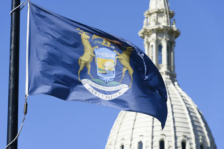 Michigan flag waving in front of the dome of the Capitol Building in downtown Lansing, the state capital.