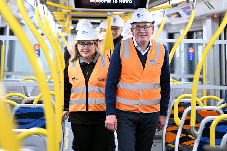 Jacinta Allan and Daniel Andrews wear hard hats and high-vis vests as the walk side by side on a train
