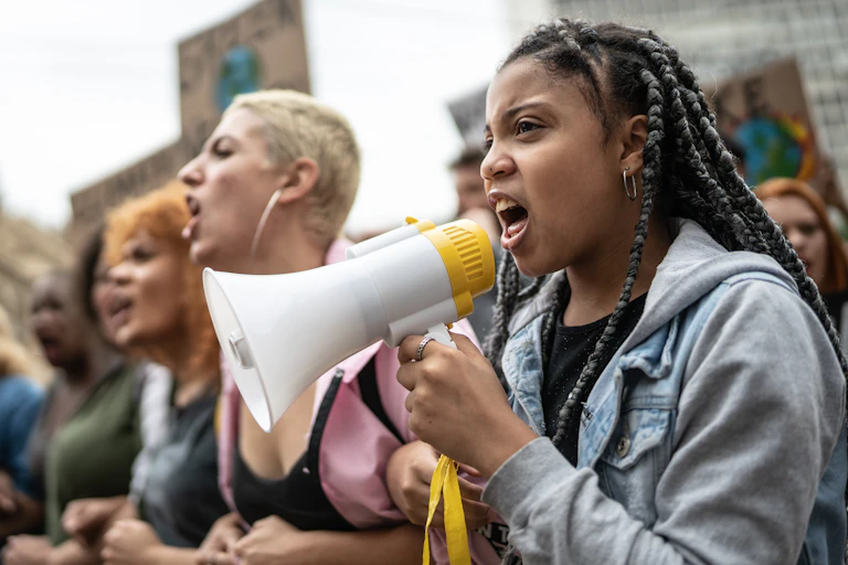 A female teenager shouts into a megaphone at a protest.