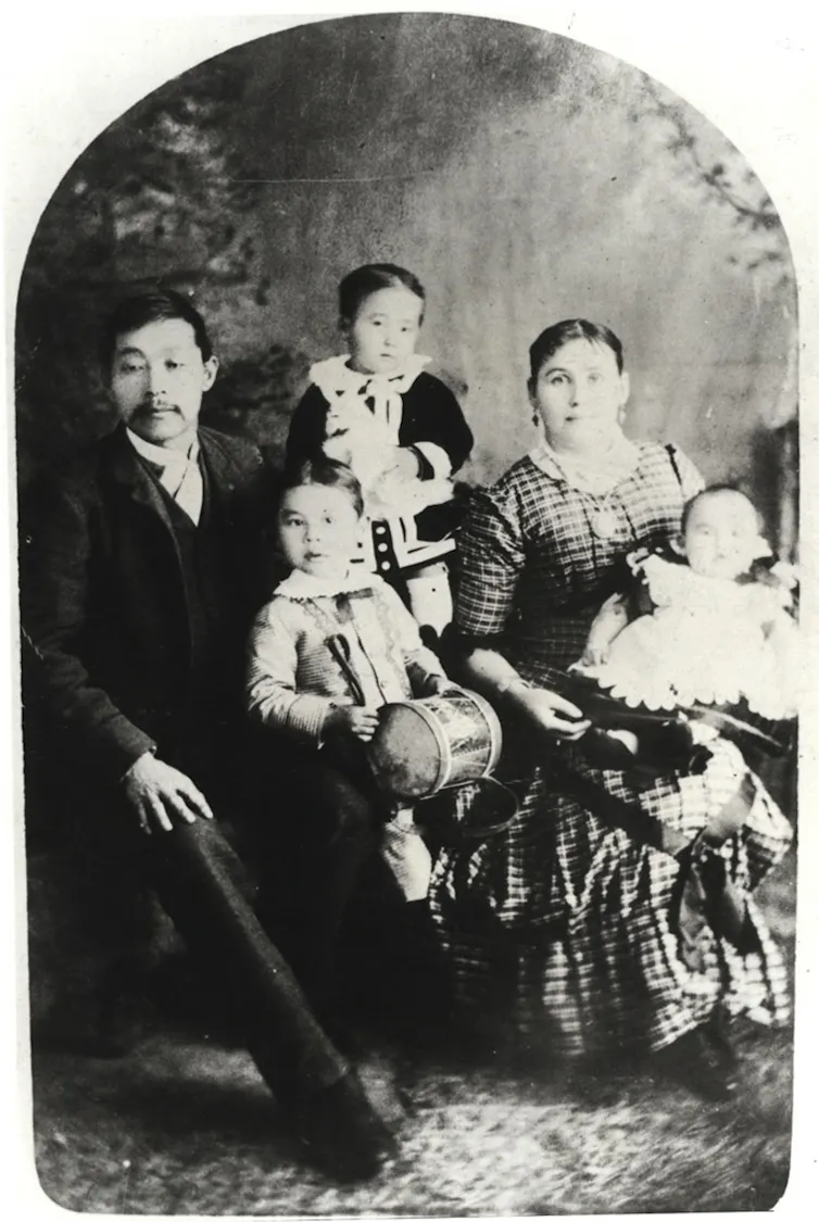 A copy of a black and white photograph of a family that consists of a Chinese man, white woman and three young children