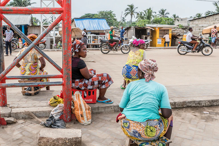 A group of women sitting in a street; motorbikes on the road