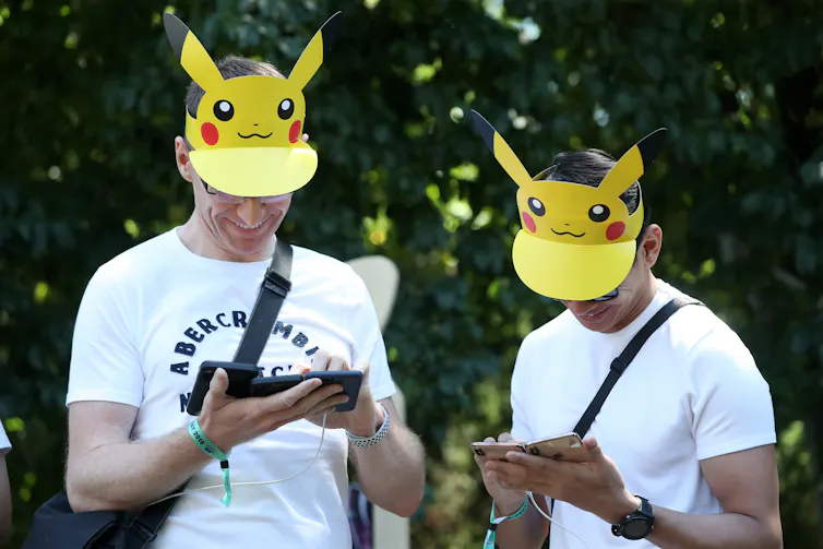 People play the Pokemon Go game on their smartphones, wearing Pikachu hats.