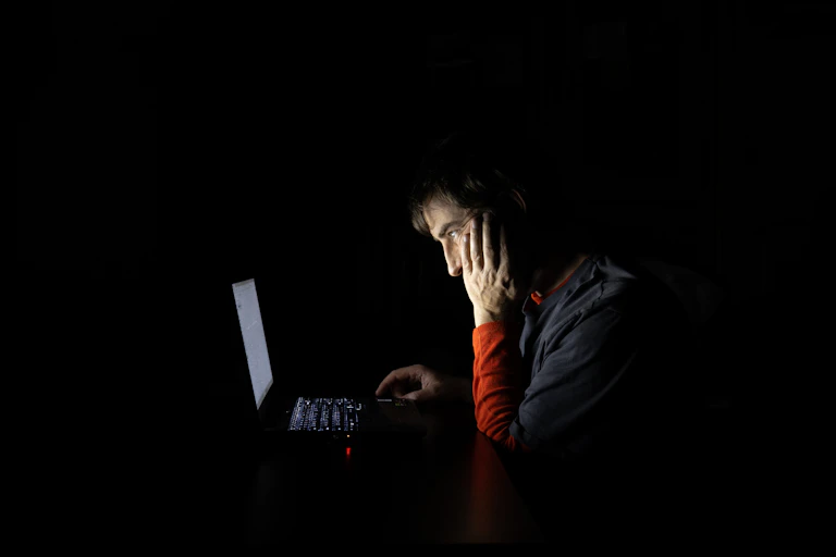 Un joven en la penumbra contempla la pantalla de un portátil