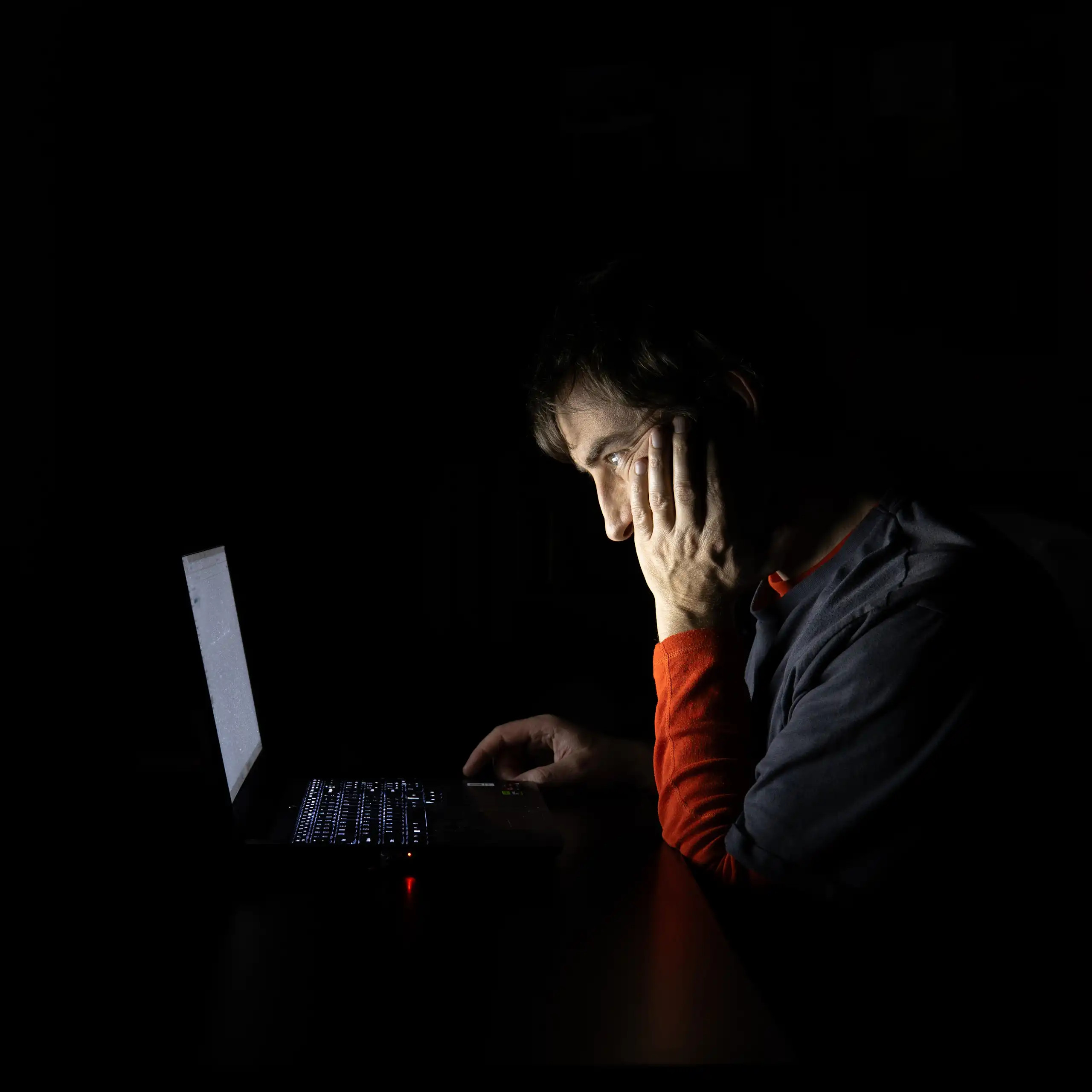 Un joven en la penumbra contempla la pantalla de un portátil