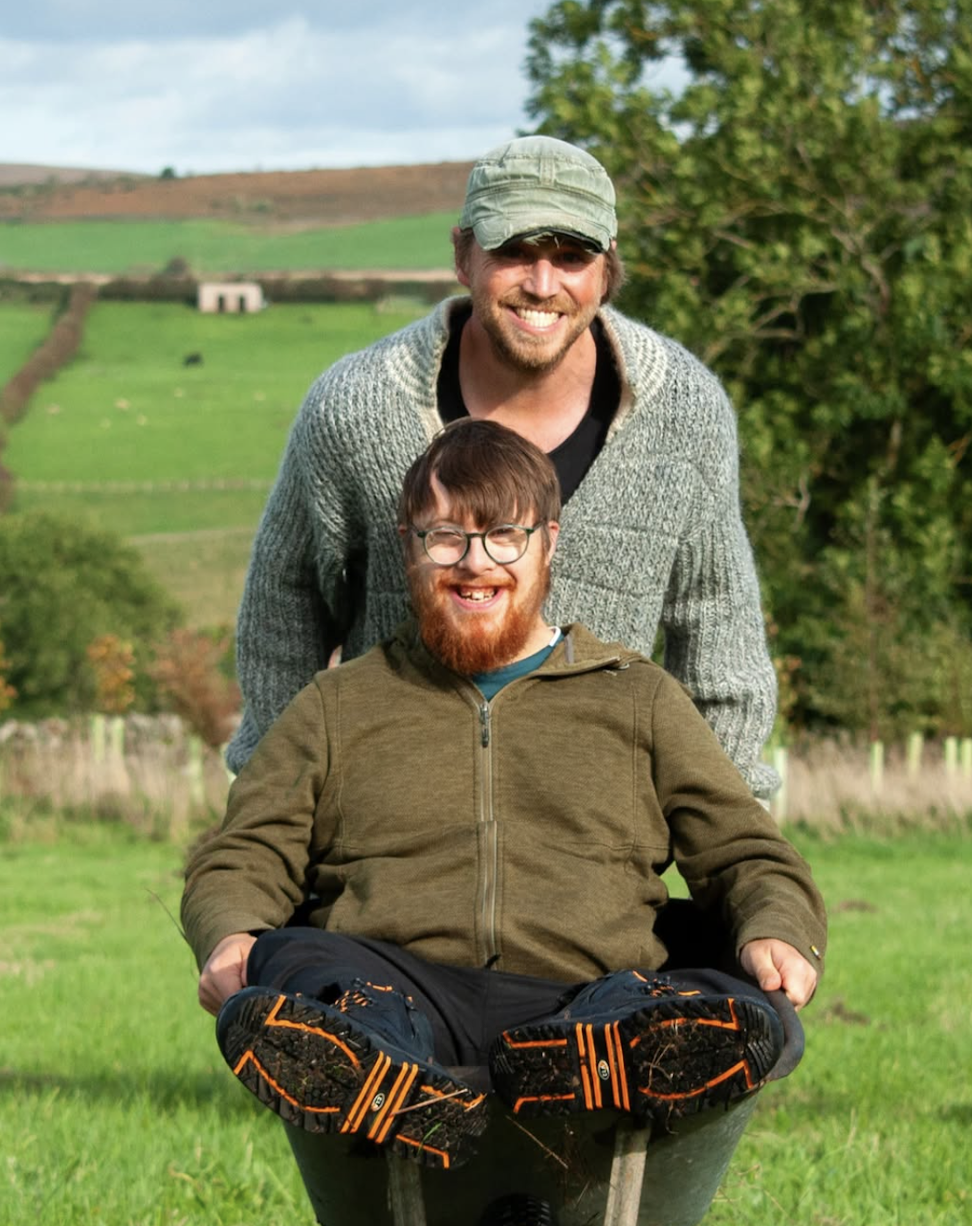 Man pushing another man in a wheelbarrow.