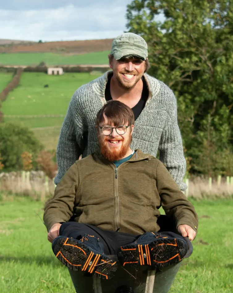 Man pushing another man in a wheelbarrow.