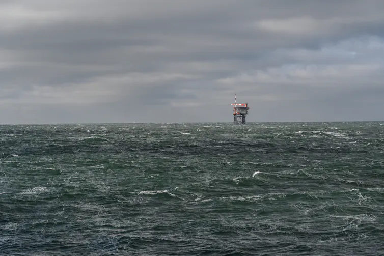 A large industrial tower rises out of a gray seascape.