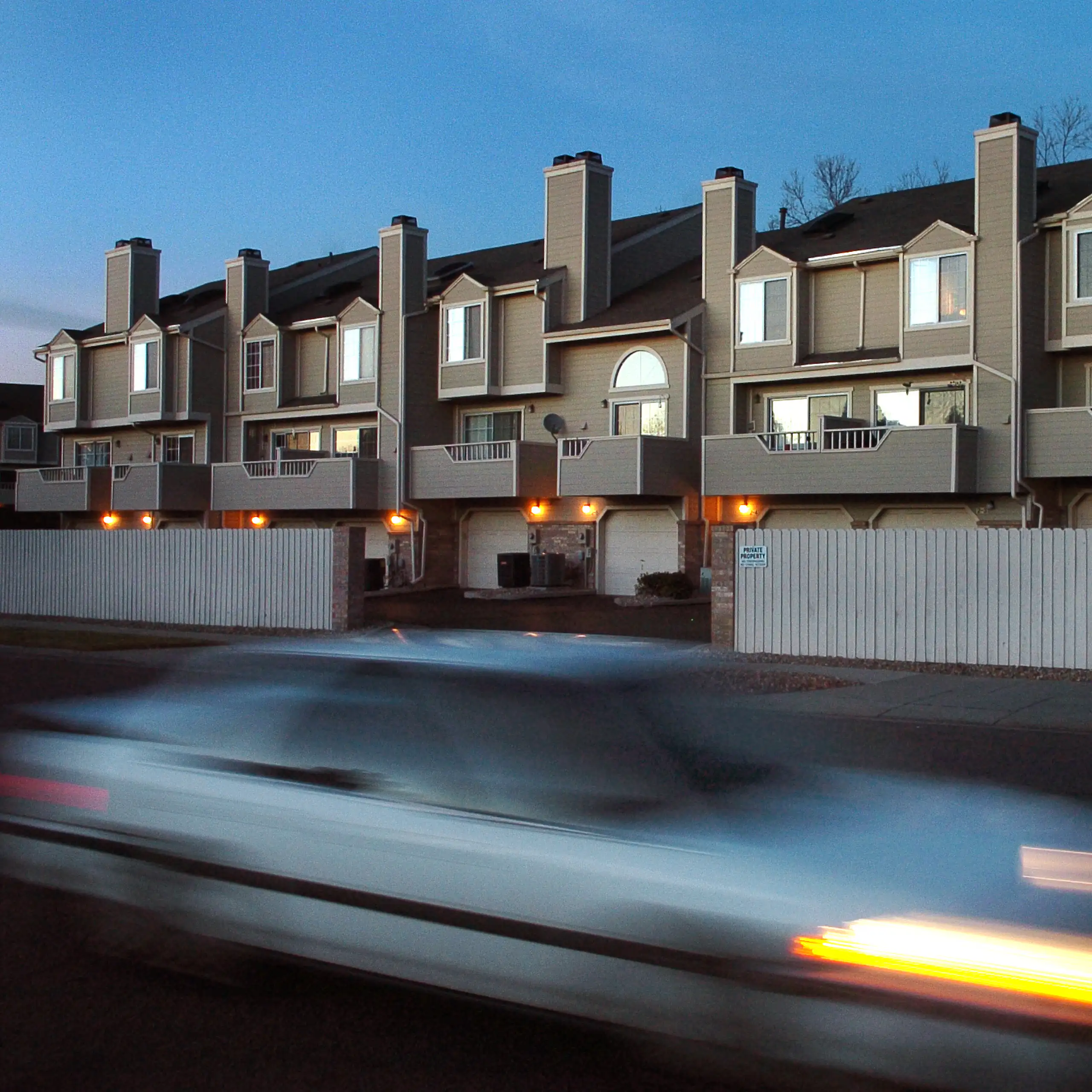A car appears blurry as it speeds by a housing complex made up of attached, tan units.