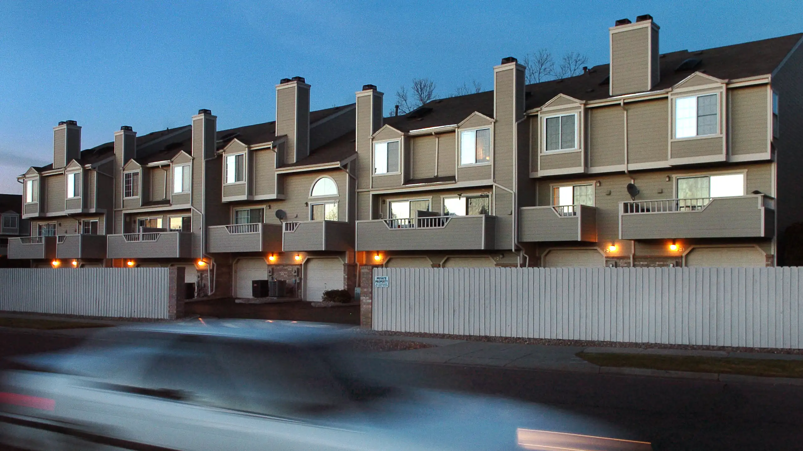 A car appears blurry as it speeds by a housing complex made up of attached, tan units.