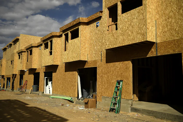 The wooden structural frame of townhomes lines a street, with open, square spaces for windows and garages.