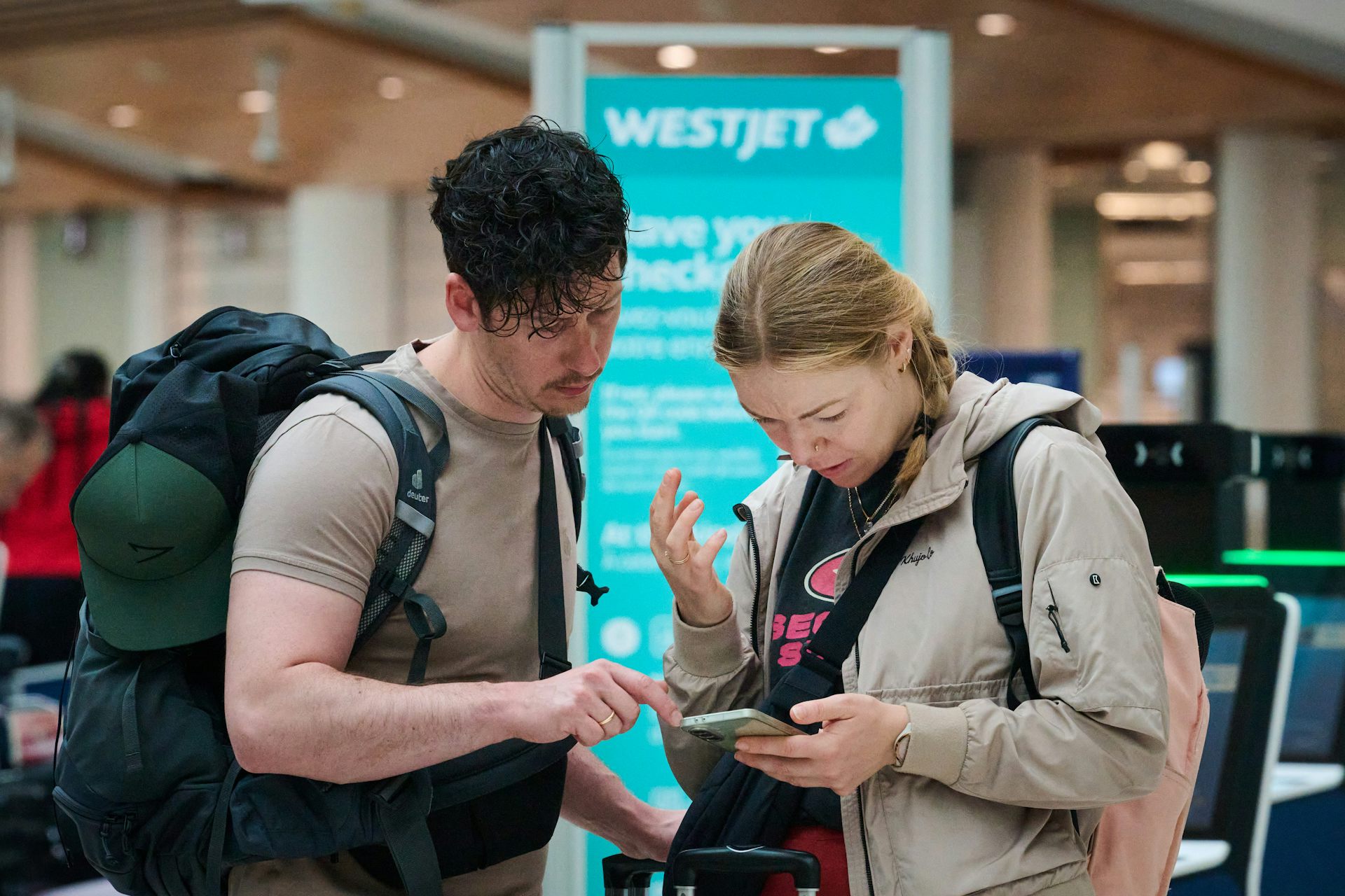 Two passengers in an airport look down at a phone