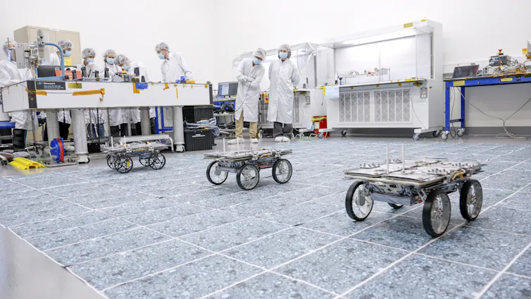 Three small robotic rovers drive across a sterile warehouse floor.