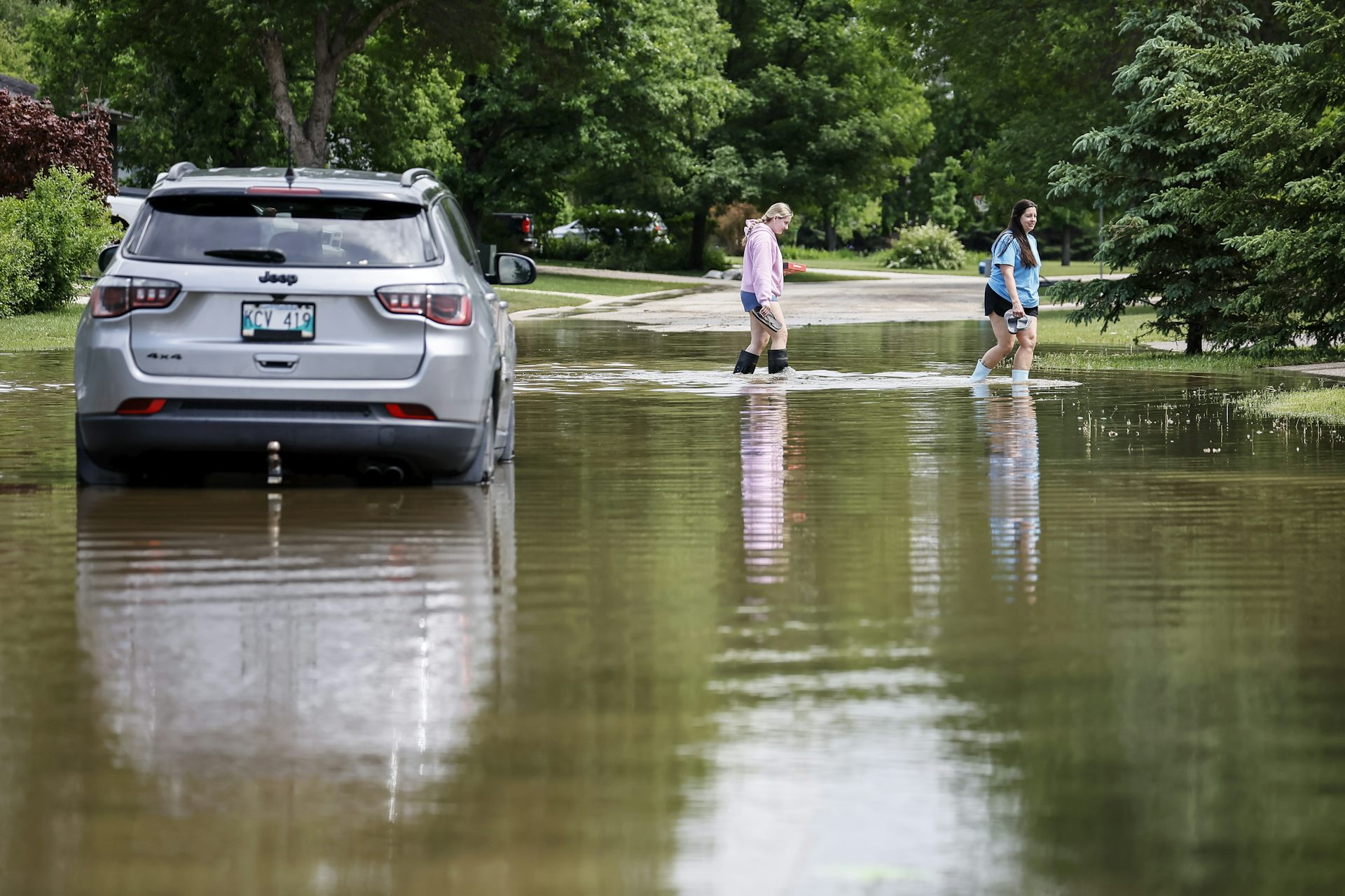 People walk by a flooded and abandoned vehicle on a street