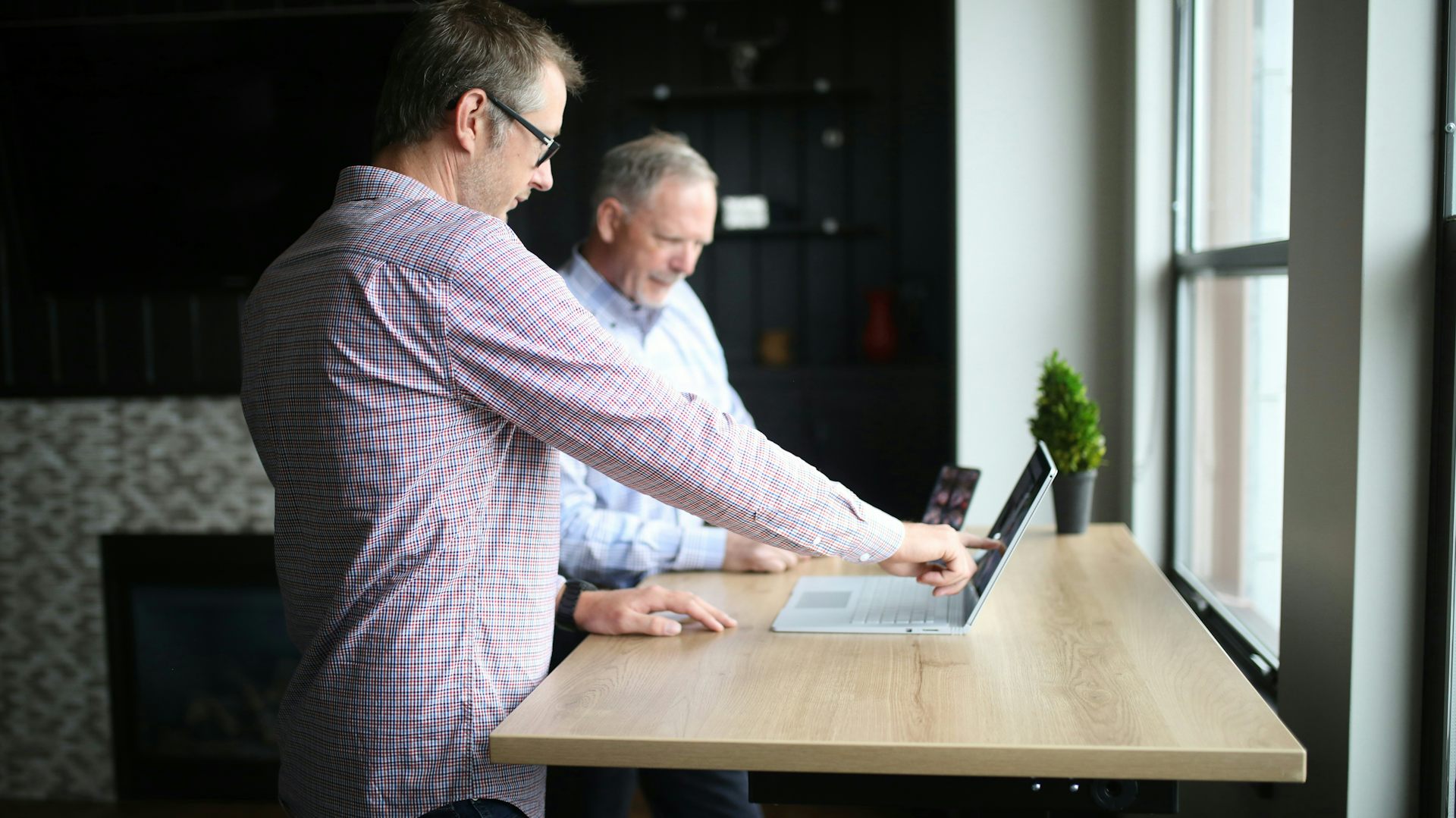 A middle-aged man points out something on a computer screen to an older man
