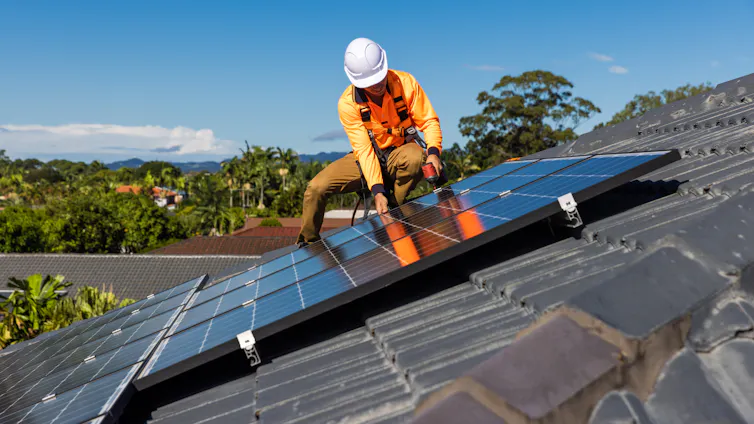 solar installer on a roof installing solar panels, forest behind.