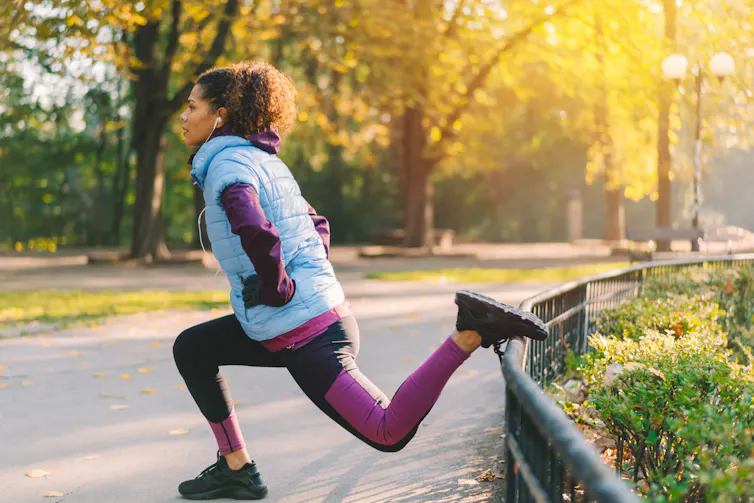 A woman does a Bulgarian split squat in a park.