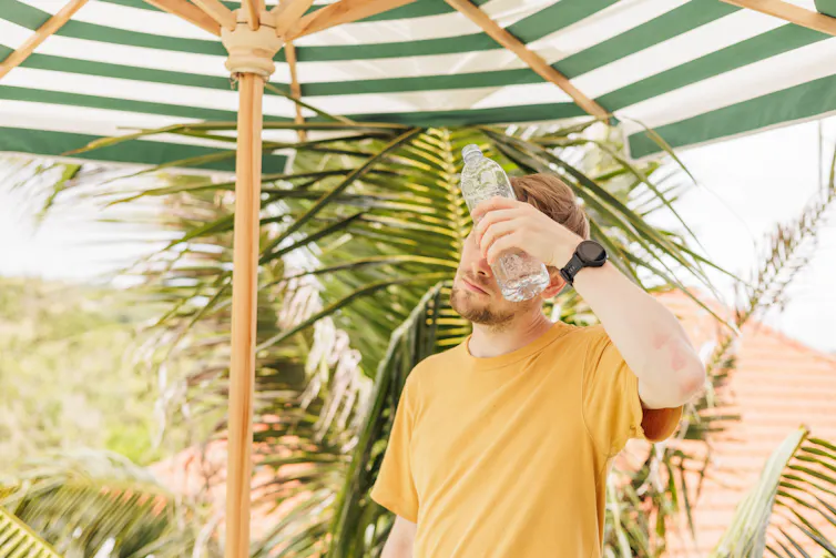 A man holds a water bottle to his head in an attempt to cool off.