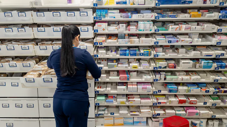 A pharmacist in front of shelves of medications.