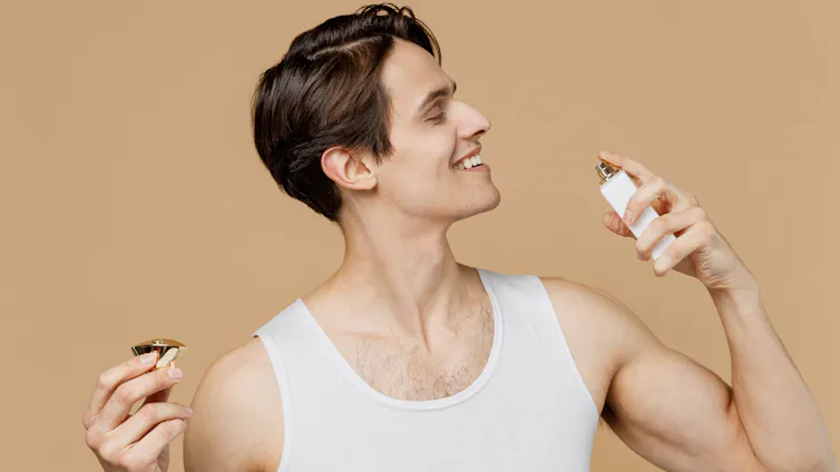 Smiling man squirts fragrance on neck