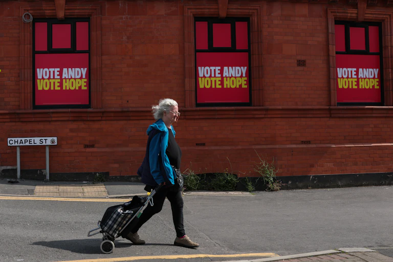 a woman walks in front of posters saying vote andy vote hope in the lead up to the makerfield byelection.
