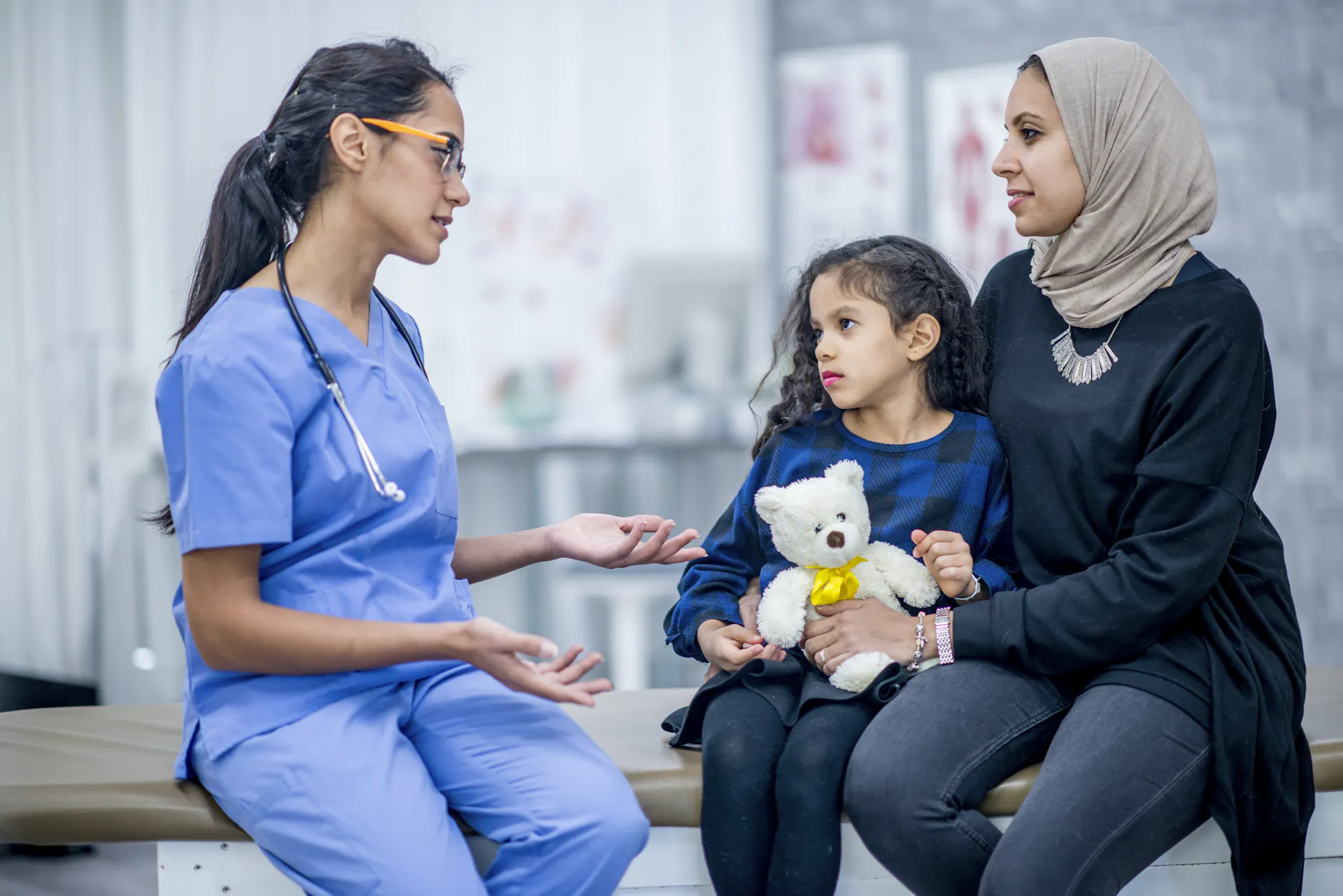 A doctor talks with a mom and her daughter in an exam room.