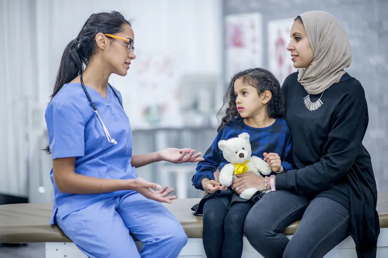 A doctor talks with a mom and her daughter in an exam room.