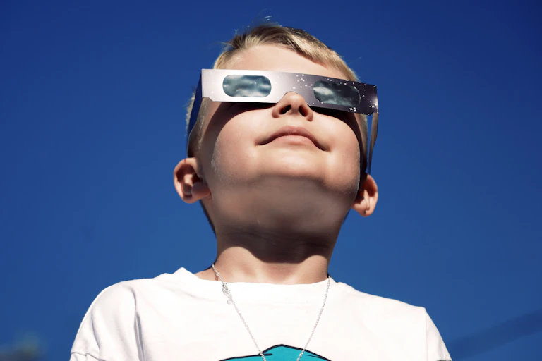 A young boy safely looks at a total eclipse while wearing protective glasses
