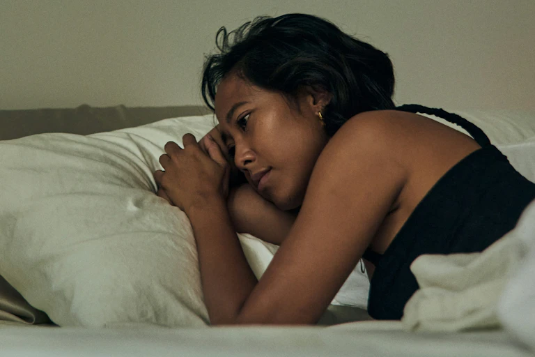 A close-up of a woman in bed looking unhappy.